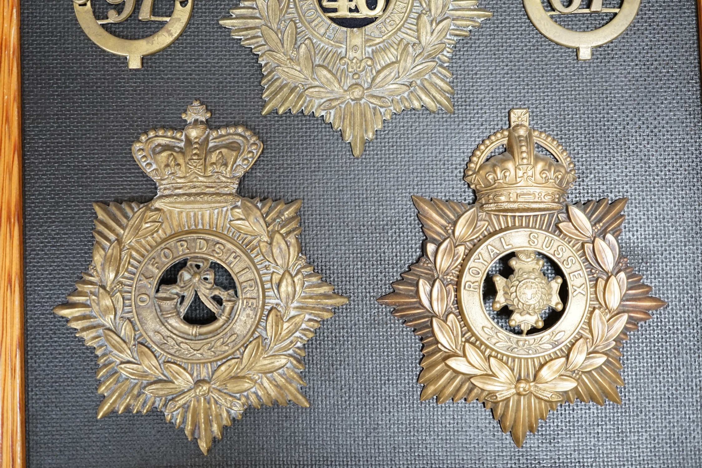 Five military helmet plates and two other centre badges mounted on a board, including; the Royal Lancashire Regiment, the Royal Lancashire 1st Volunteer Battalion, the Oxfordshire Regiment, the Royal Sussex Regiment, etc